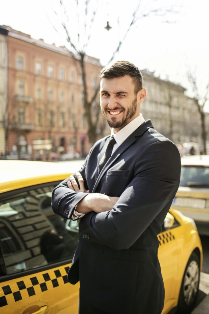 pexels photo 3777563 3777563 A confident businessman in formal attire stands smiling by a yellow taxi on a sunny day.
