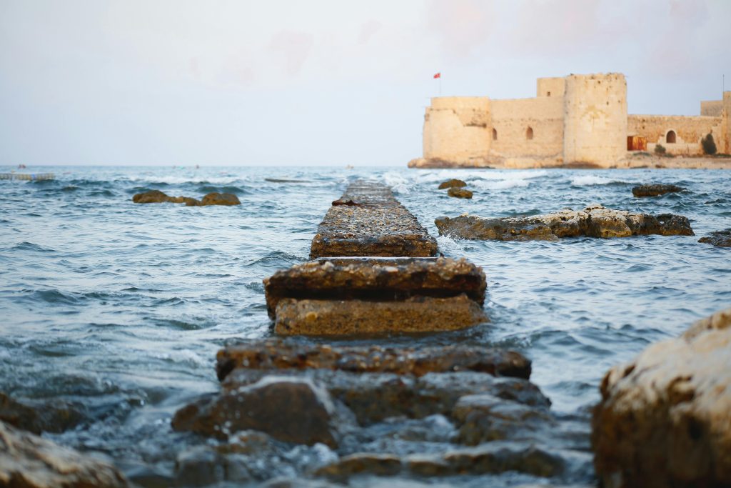 pexels photo 34835233 34835233 Ancient castle overlooking the sea with a stone path leading into the water, serene blue tones.